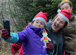 Photo of three girls taking a selfie while holding a paper christmas elf. 